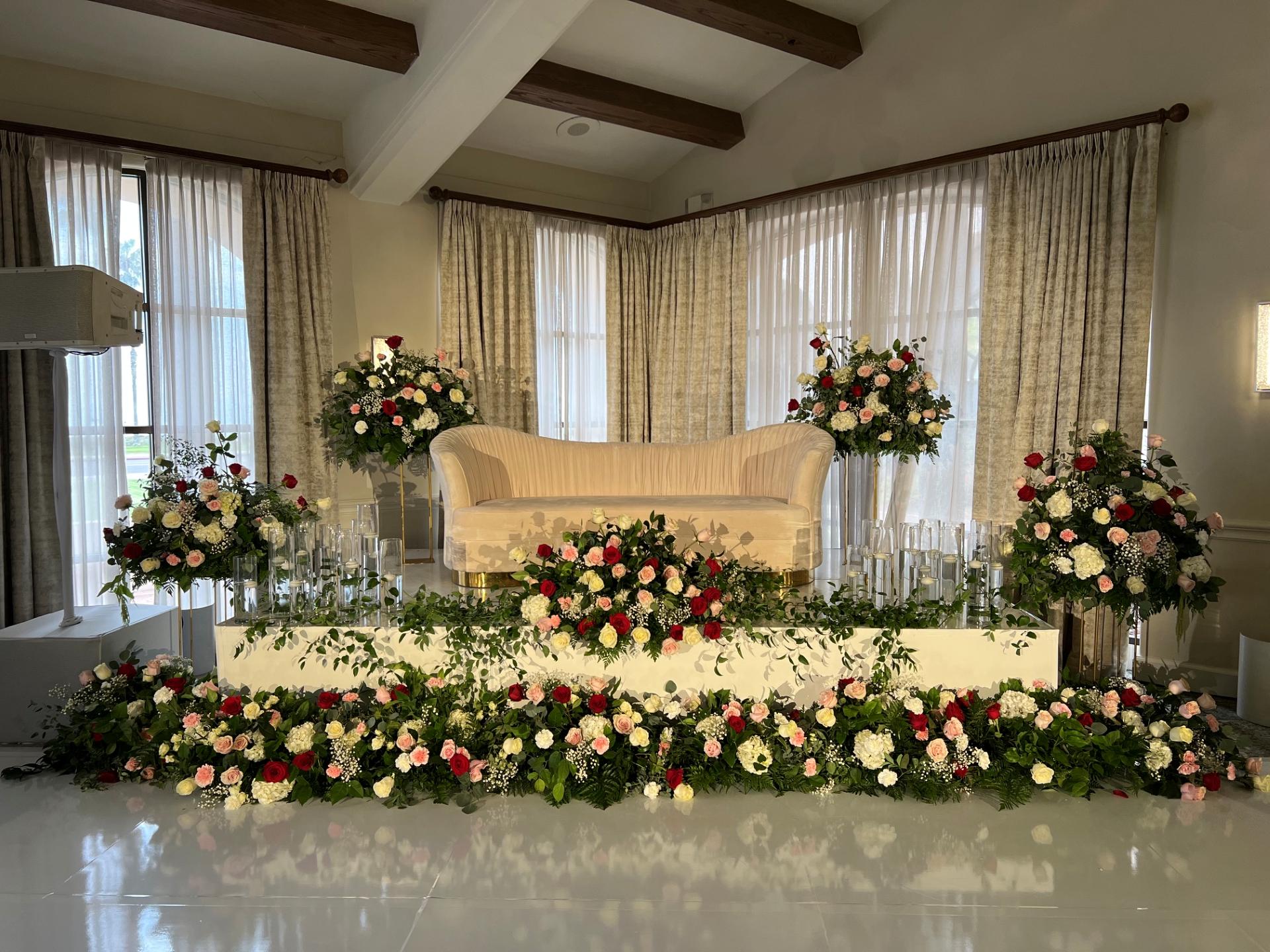 Cream sweetheart sofa surrounded by elaborate red, blush, and white floral arrangements, greenery, and clear candleholders.