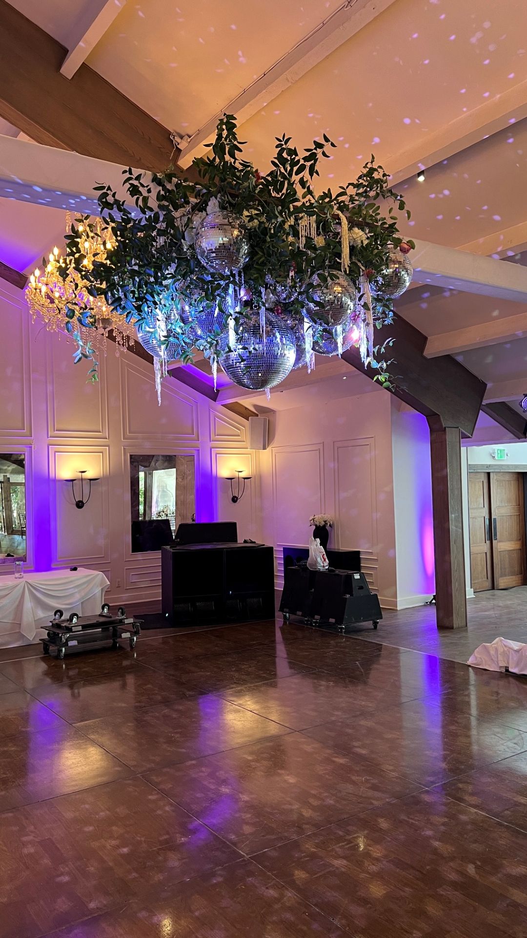 Ceiling installation of greenery, hanging disco balls, crystal accents, and dramatic purple event lighting above a dance floor.