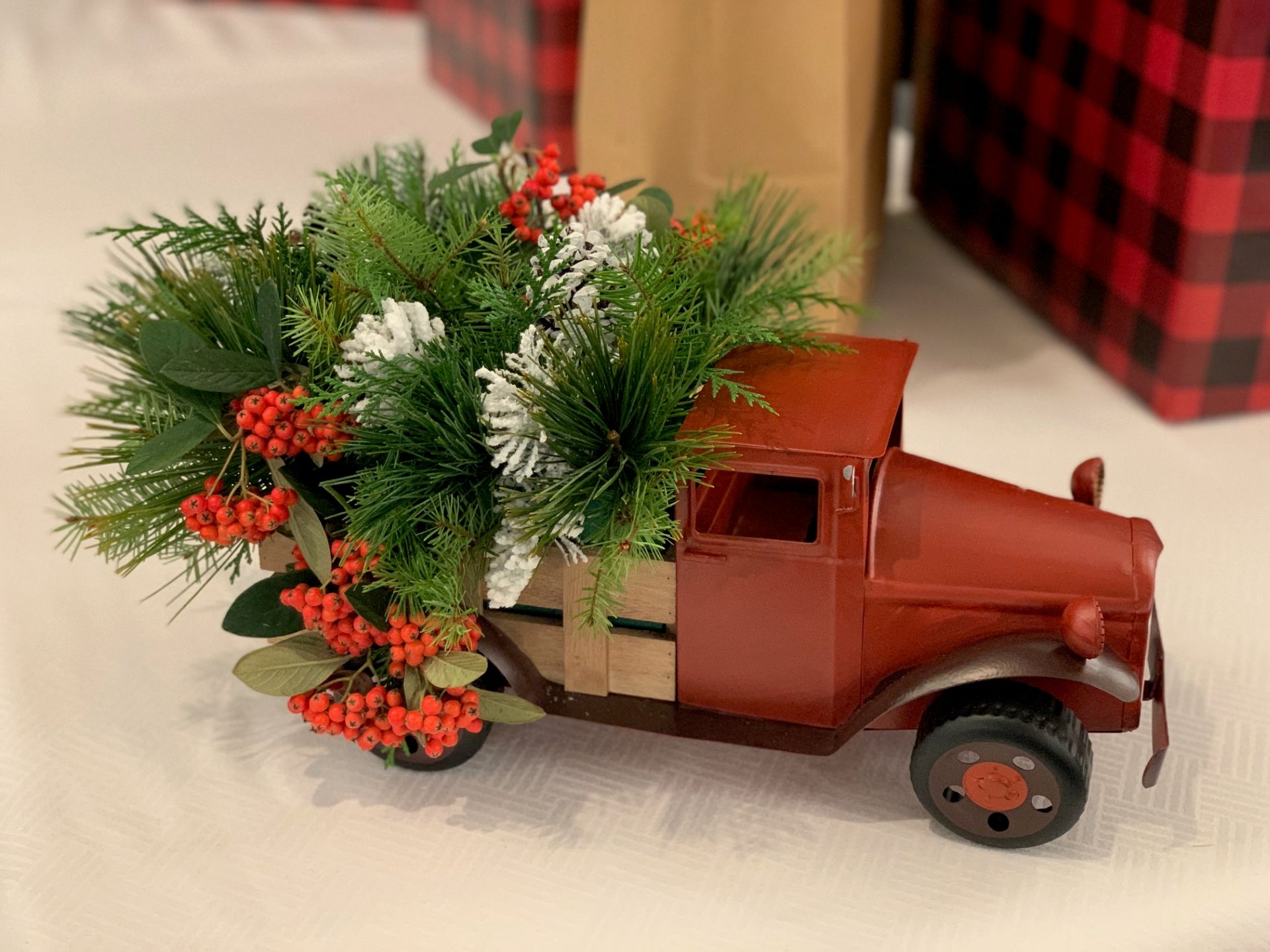 Rustic red truck centerpiece filled with evergreen branches, frosted pinecones, and bright red berries.