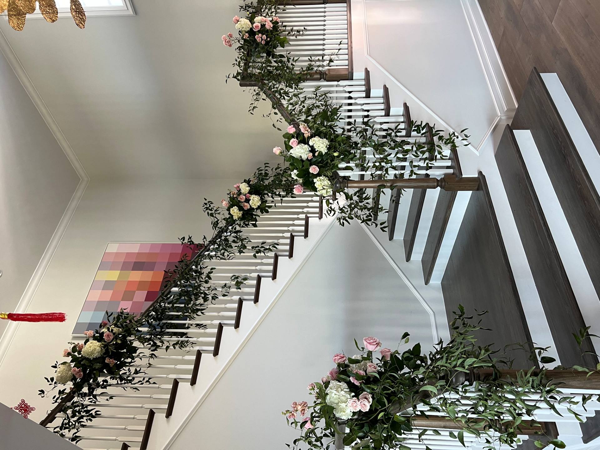 Staircase decorated with cascading greenery and soft pink and white floral arrangements along the railing.