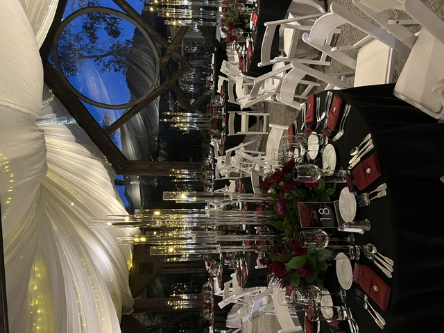 Evening reception beneath draped fabric and string lights with black table linens, tall candle centerpieces, and deep red floral arrangements.