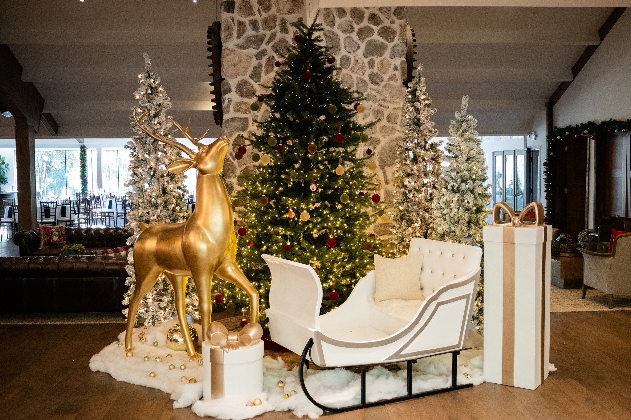 Holiday display with a large decorated Christmas tree, gold reindeer, white sleigh, and wrapped presents.