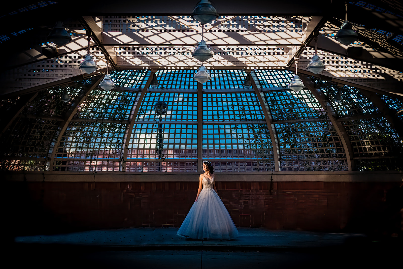 Bride posing alone beneath a dramatic geometric pavilion with blue-toned evening light.