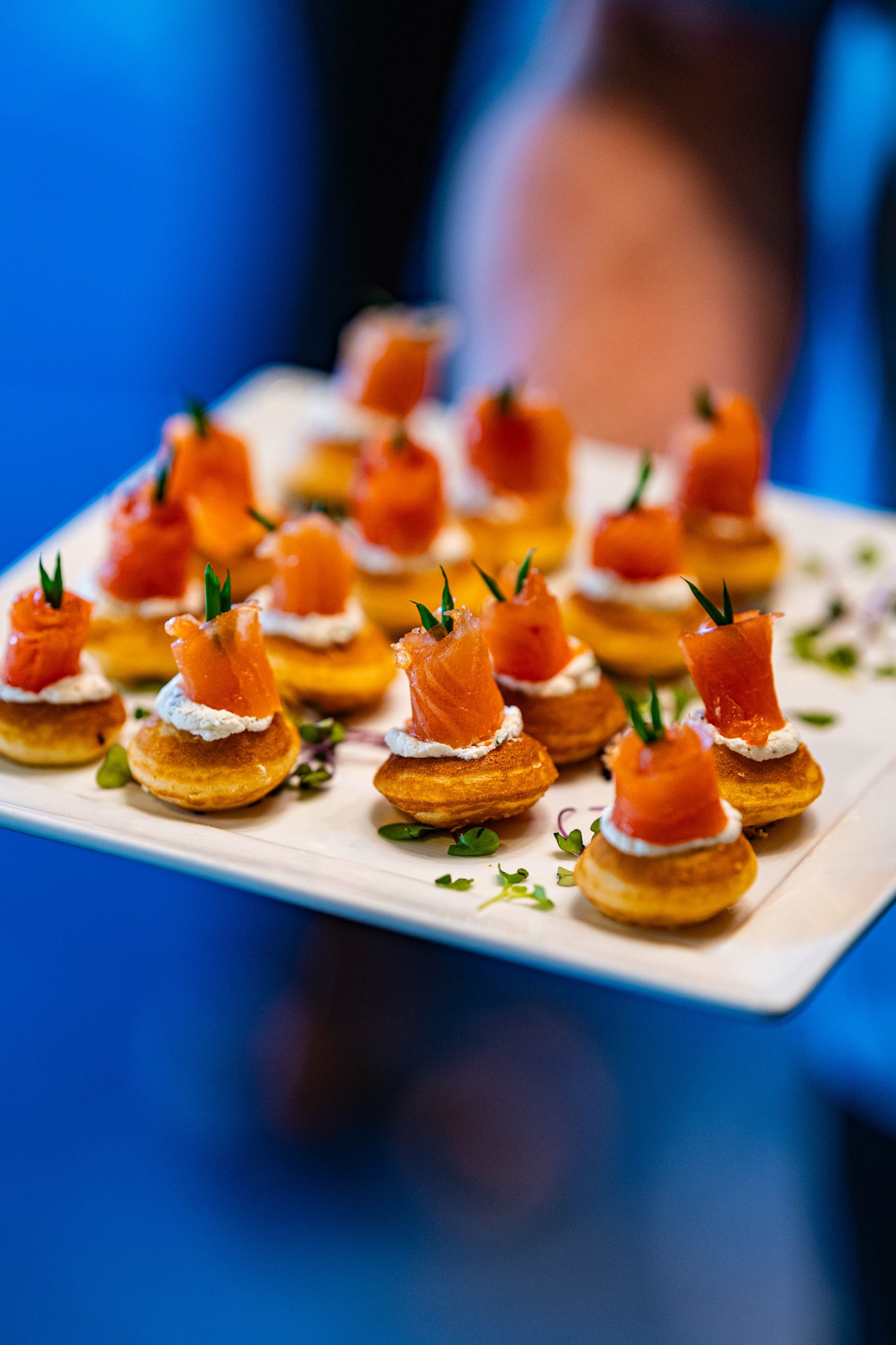 Tray of bite-sized appetizers topped with smoked salmon, cream, and fresh herbs.