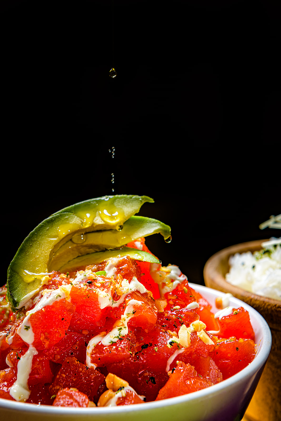 Close-up of a colorful dish topped with avocado, sauce, and seasoning against a dark background.