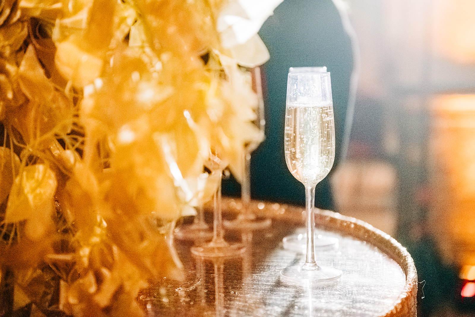 Close-up of a champagne flute filled with sparkling wine beside a warm gold-toned decorative display.