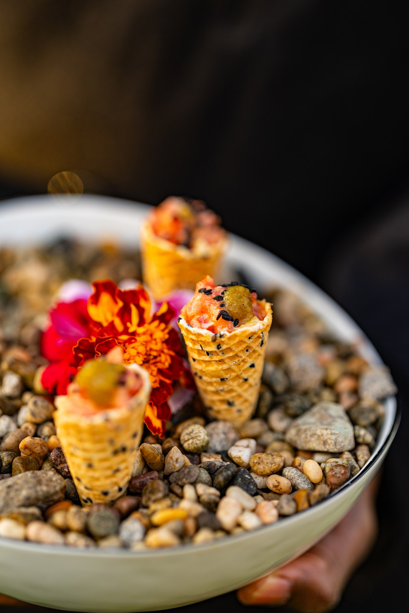 Close-up of small savory appetizer cones arranged among decorative stones and a bright red flower.