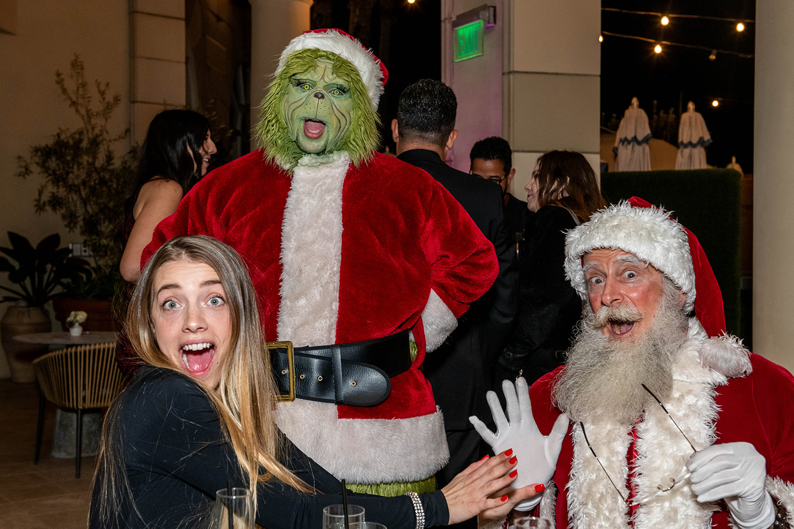 Woman posing with Santa and a Grinch character at a festive holiday party.