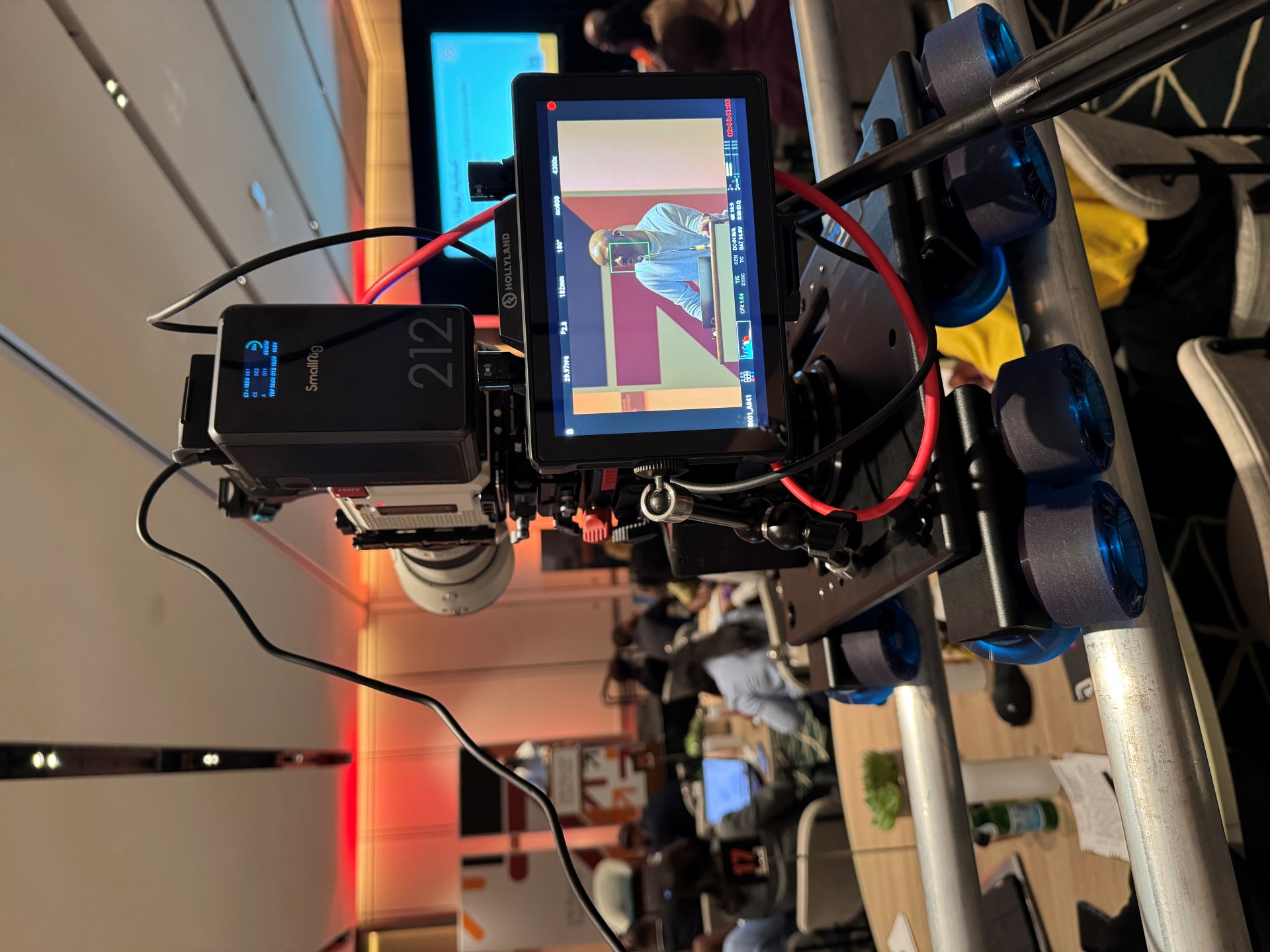 Large camera on dolly filming a keynote presentation event with a speaker on stage.