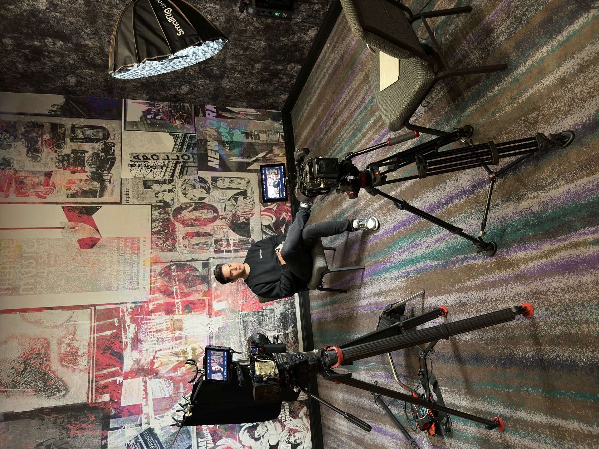 Man sitting down in a chair surrounded by lighting and cinema cameras, ready for an interview.