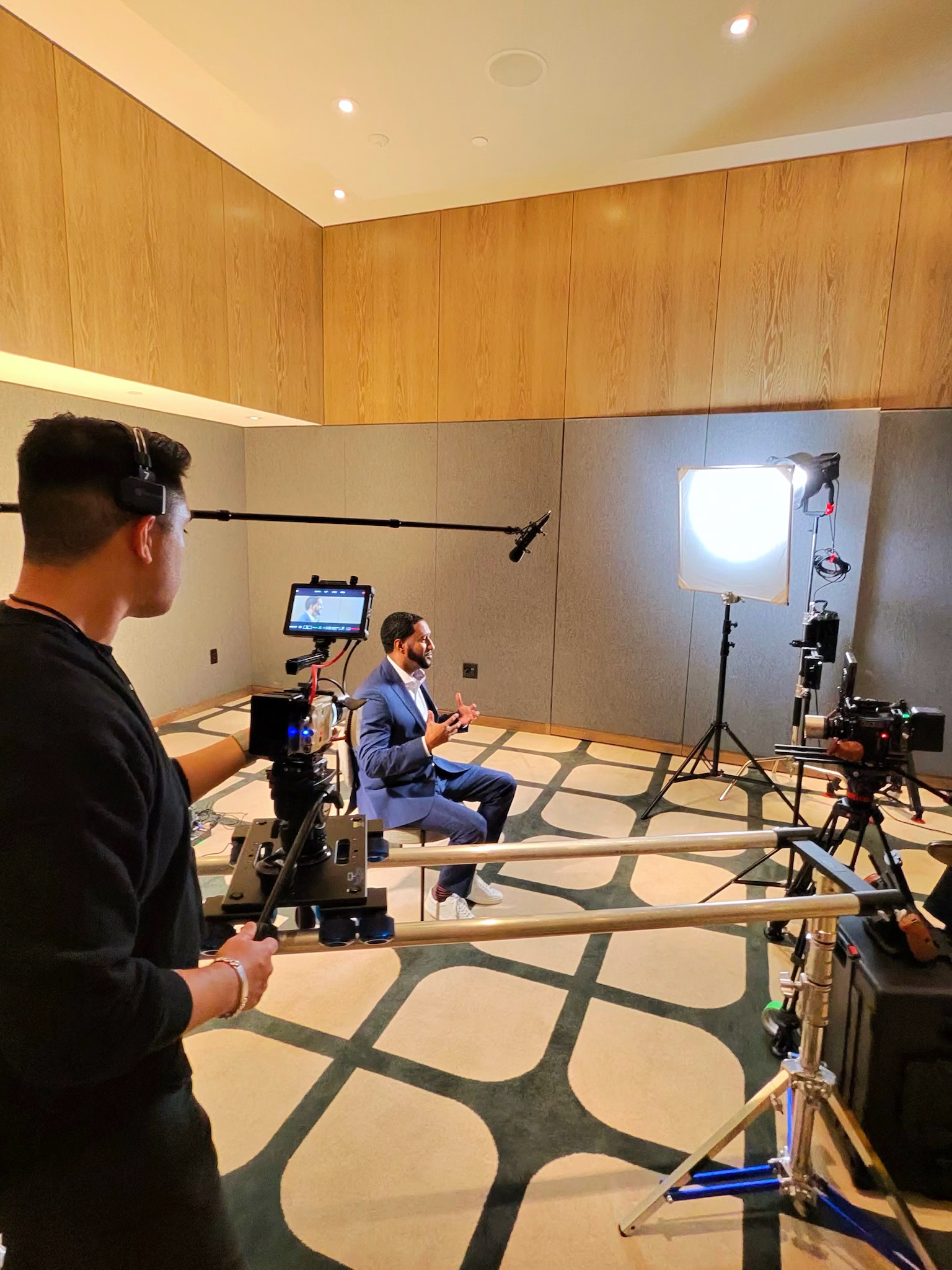 Man controlling a cinema camera on a slider dolly while filming a sit down interview with multiple cameras and lighting set up around.