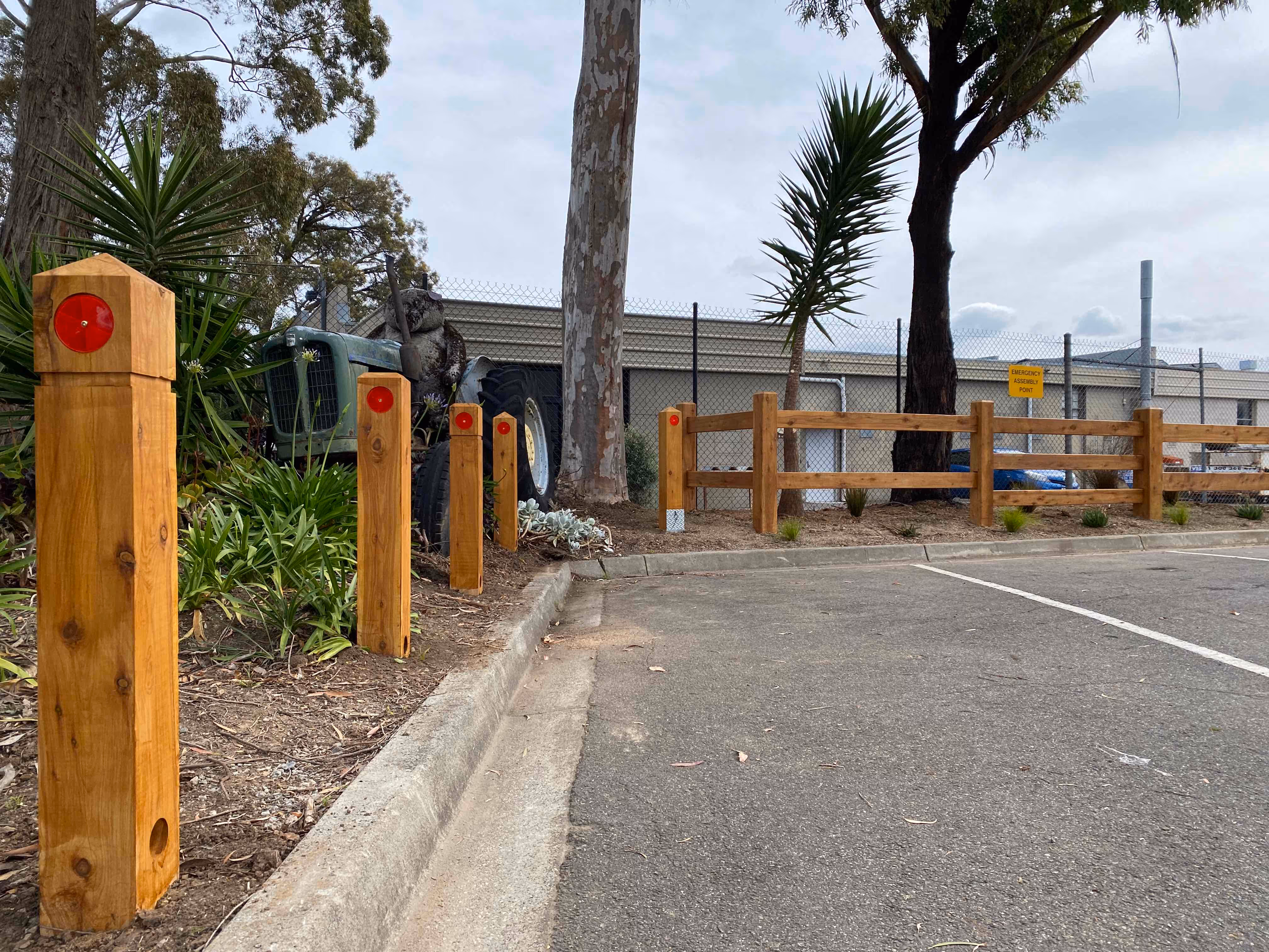 Wooden posts with red reflectors line a parking lot edge near a tractor and fence.
