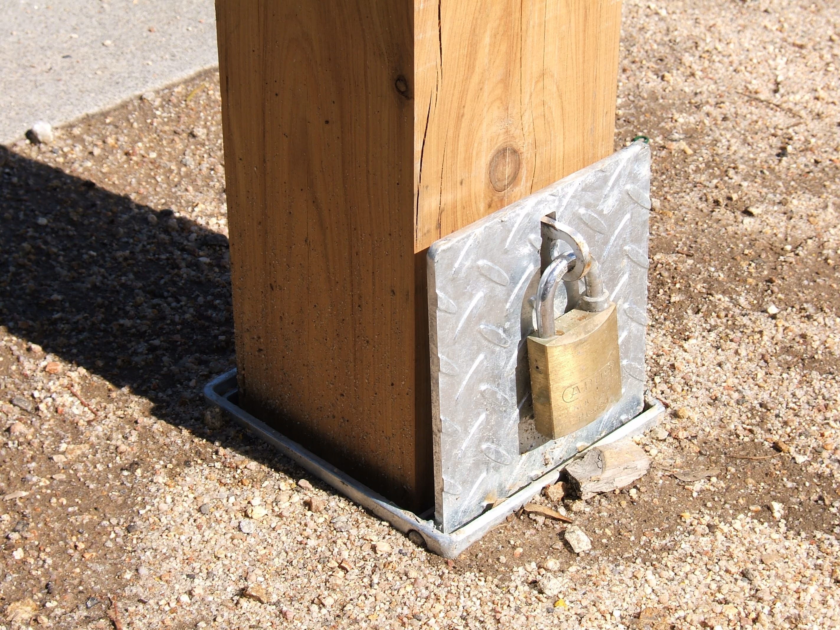 A row of wooden posts with red reflectors lined along a gravel and concrete path near modern buildings.