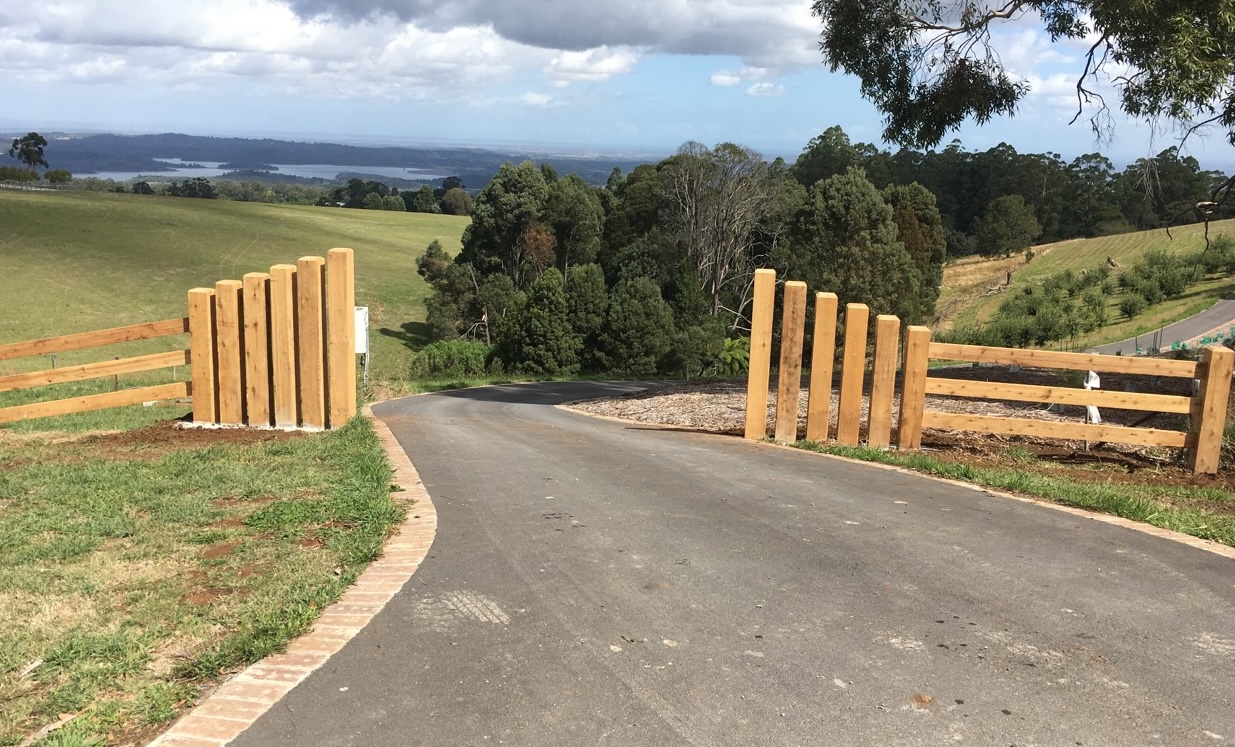 Black painted cypress post and rail fence with two rails along a paddock with horses