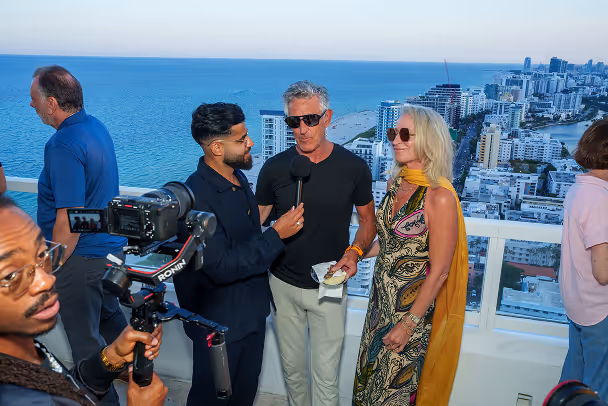 Videographer filming rooftop interview with attendees, aerial ocean and city skyline view in background