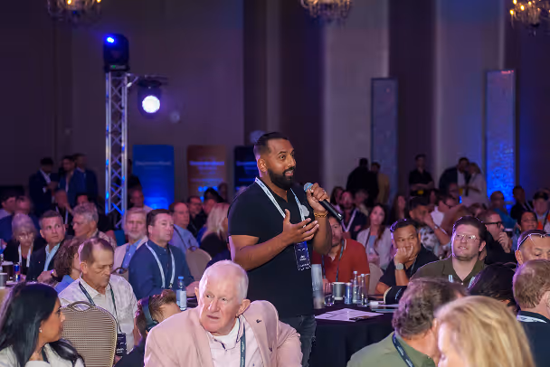 Attendee standing with microphone among packed conference audience in grand ballroom during session