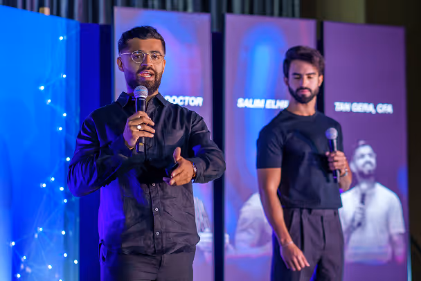 Two speakers presenting on stage with microphones in front of blue LED backdrop at conference