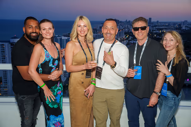 Six attendees posing together on rooftop terrace at sunset with city skyline and ocean in background