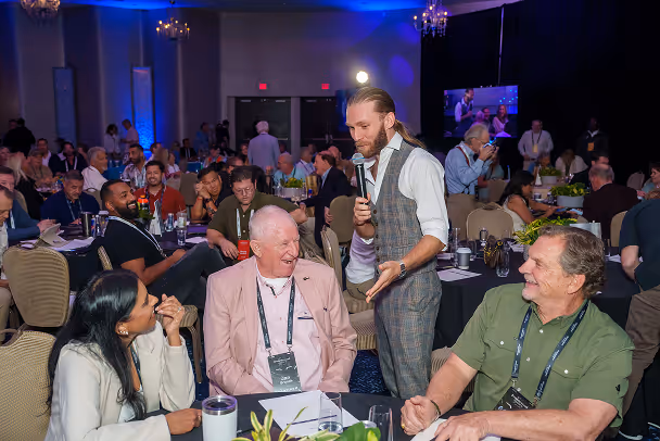 Facilitator with microphone engaging with laughing attendees at conference tables in large ballroom