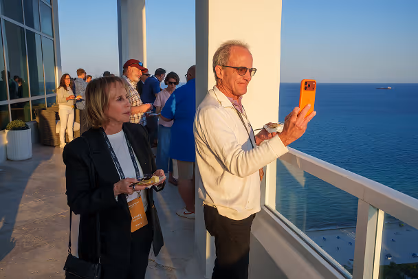 Speaker and attendee posing together at networking reception, event hall with guests in background