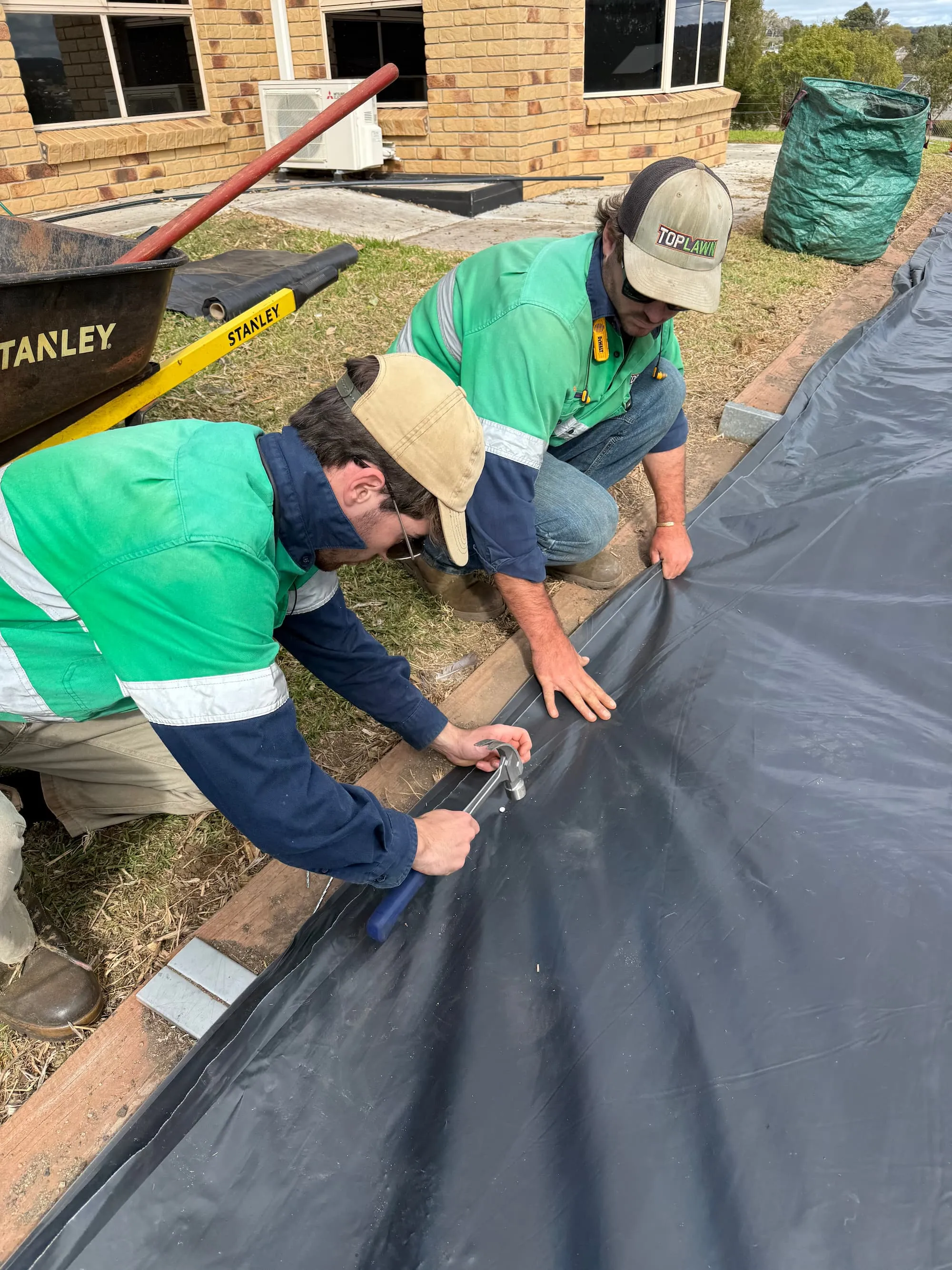 Zac and Tom from TopLawn installing black plastic underlay for a rock bed