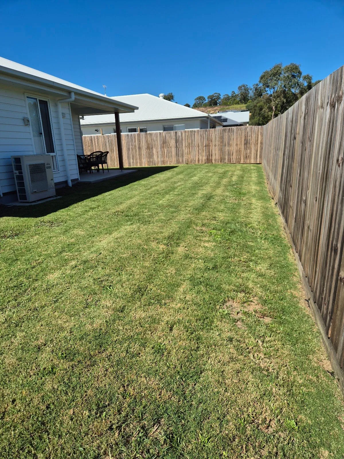 The same side yard after mowing, with even stripes along the fence