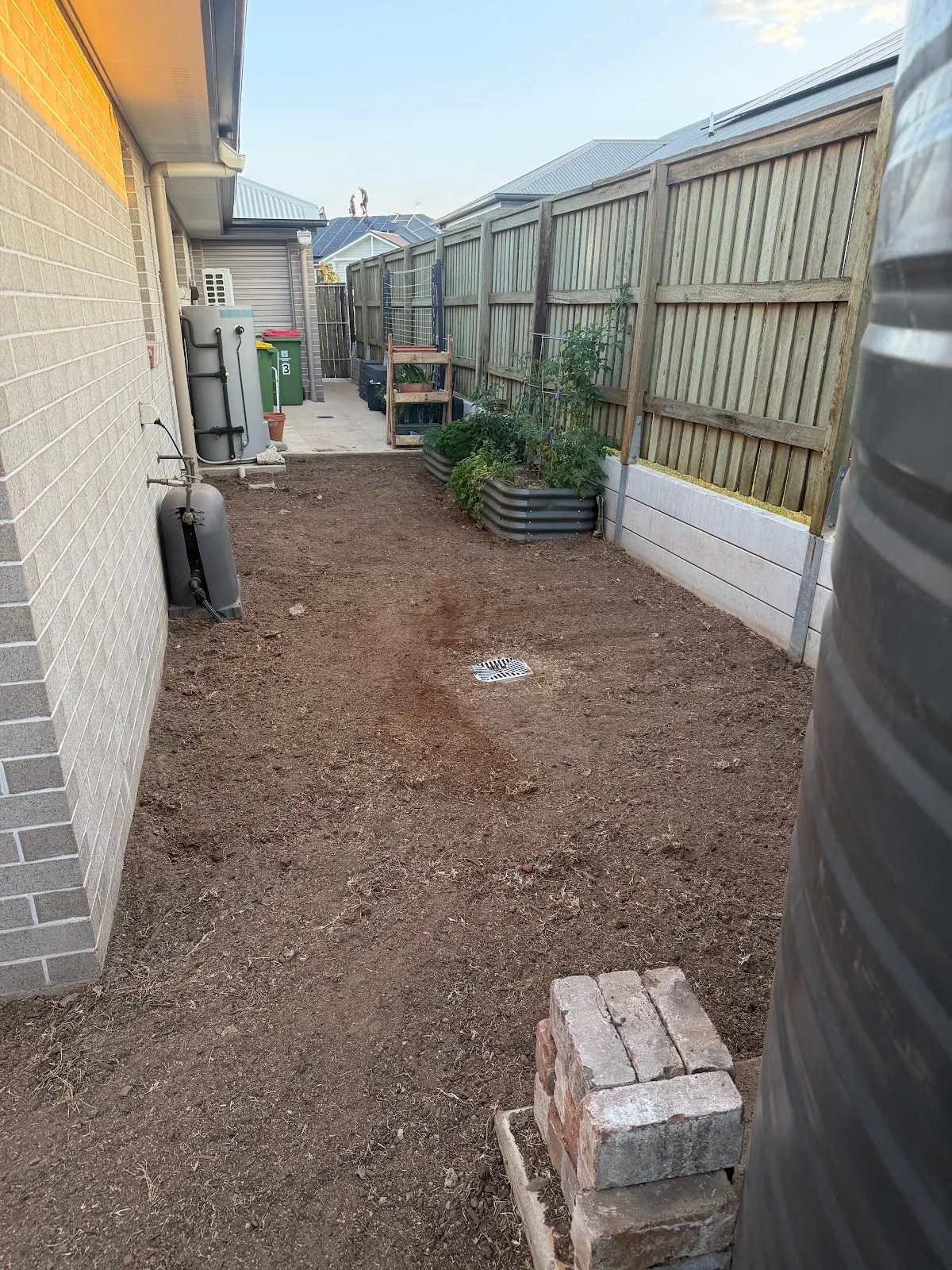 Side yard cleared back to bare soil beside a water tank