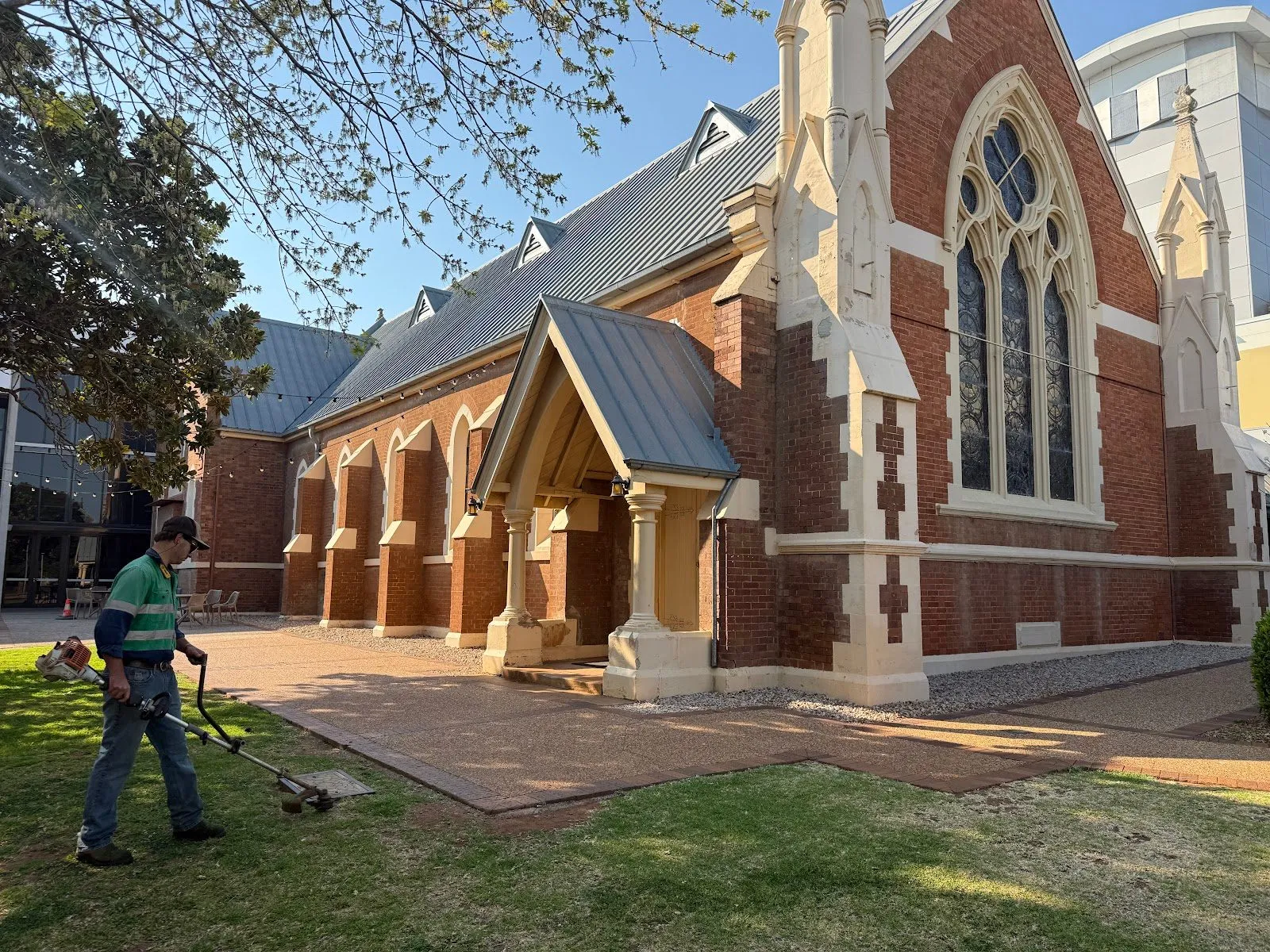 TopLawn crew member whipper-snipping the lawn edges beside a heritage brick church