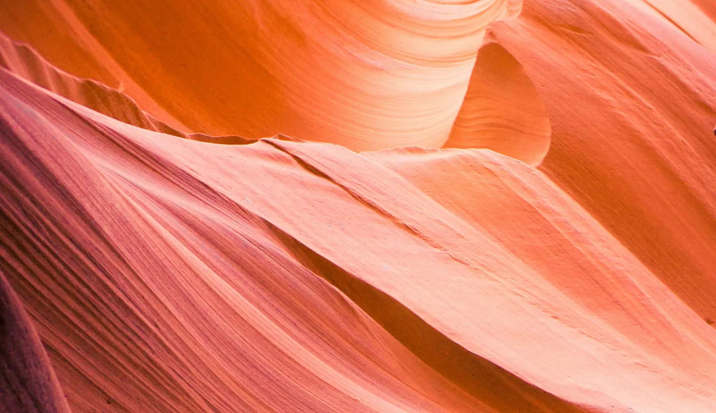 Smooth, flowing orange and pink rock formations with layered textures in a canyon.