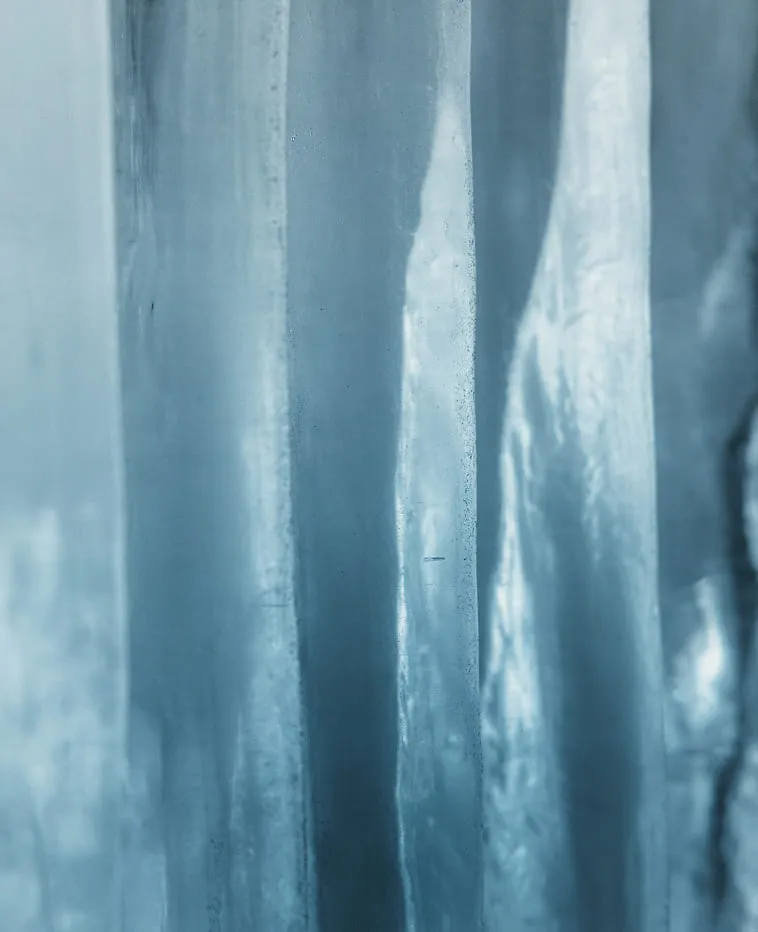 Close-up of vertical translucent blue ice columns with light reflections and texture.