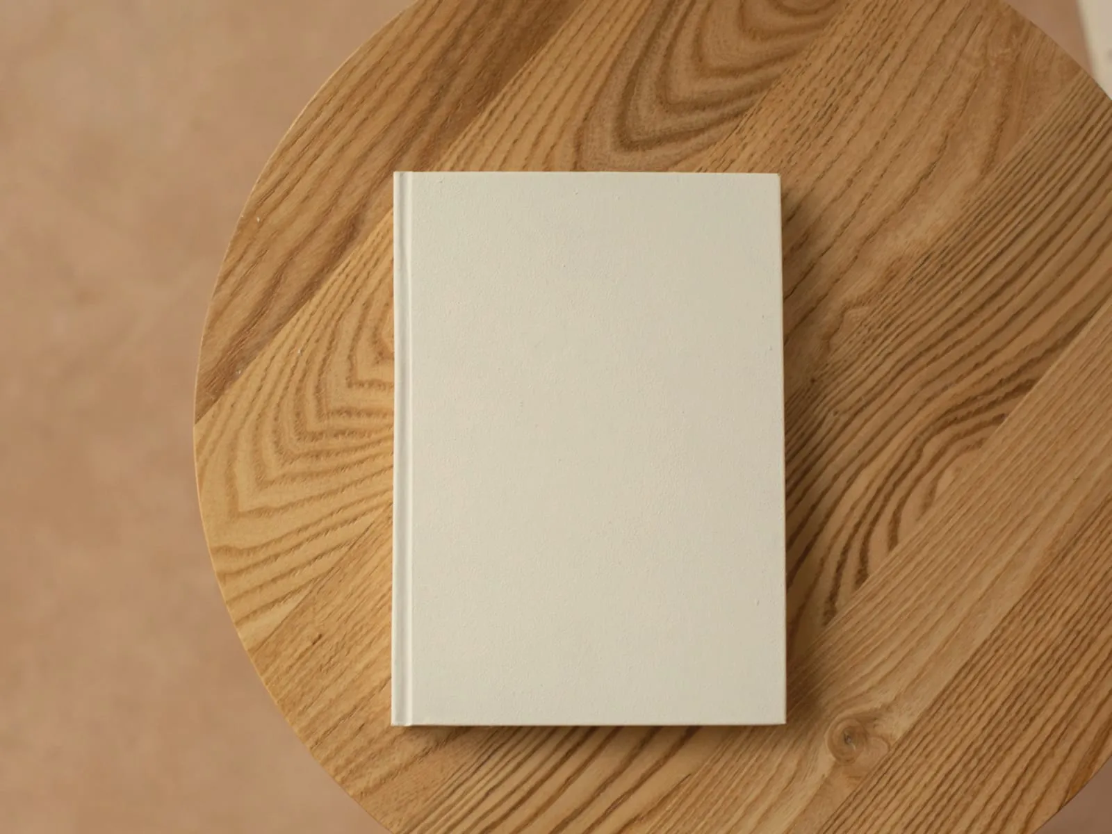 Ein geschlossenes cremefarbenes Notizbuch liegt auf einer runden Tischplatte aus Eiche