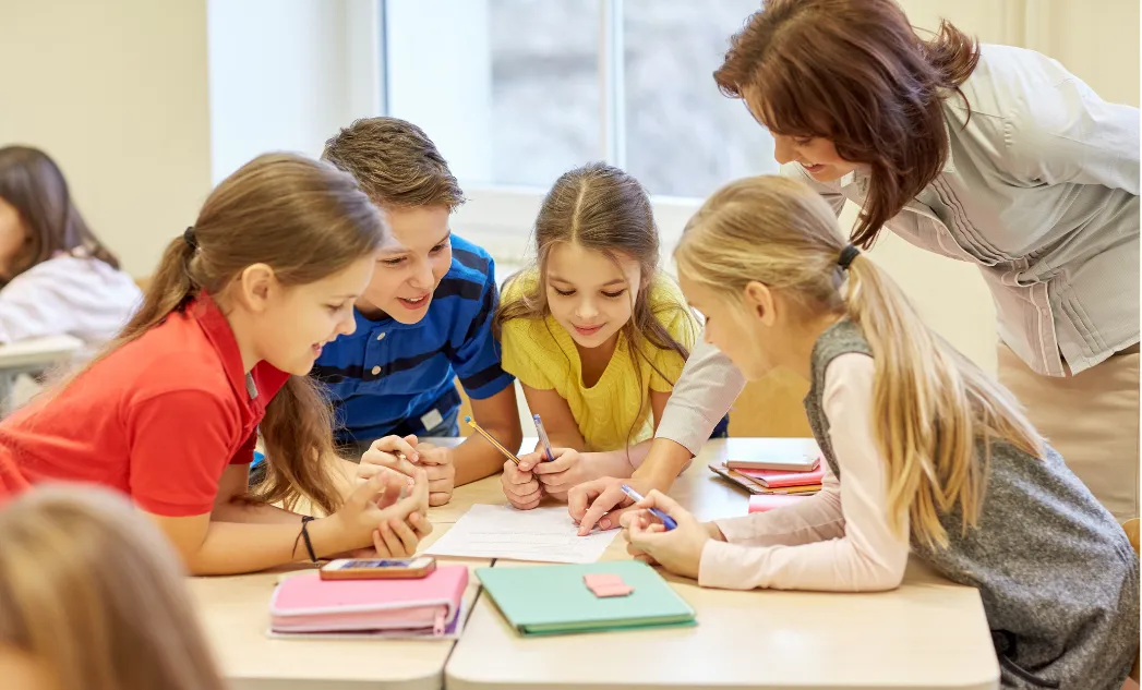 Eine Lehrerin beugt sich über einen Gruppentisch, an dem vier Kinder arbeiten