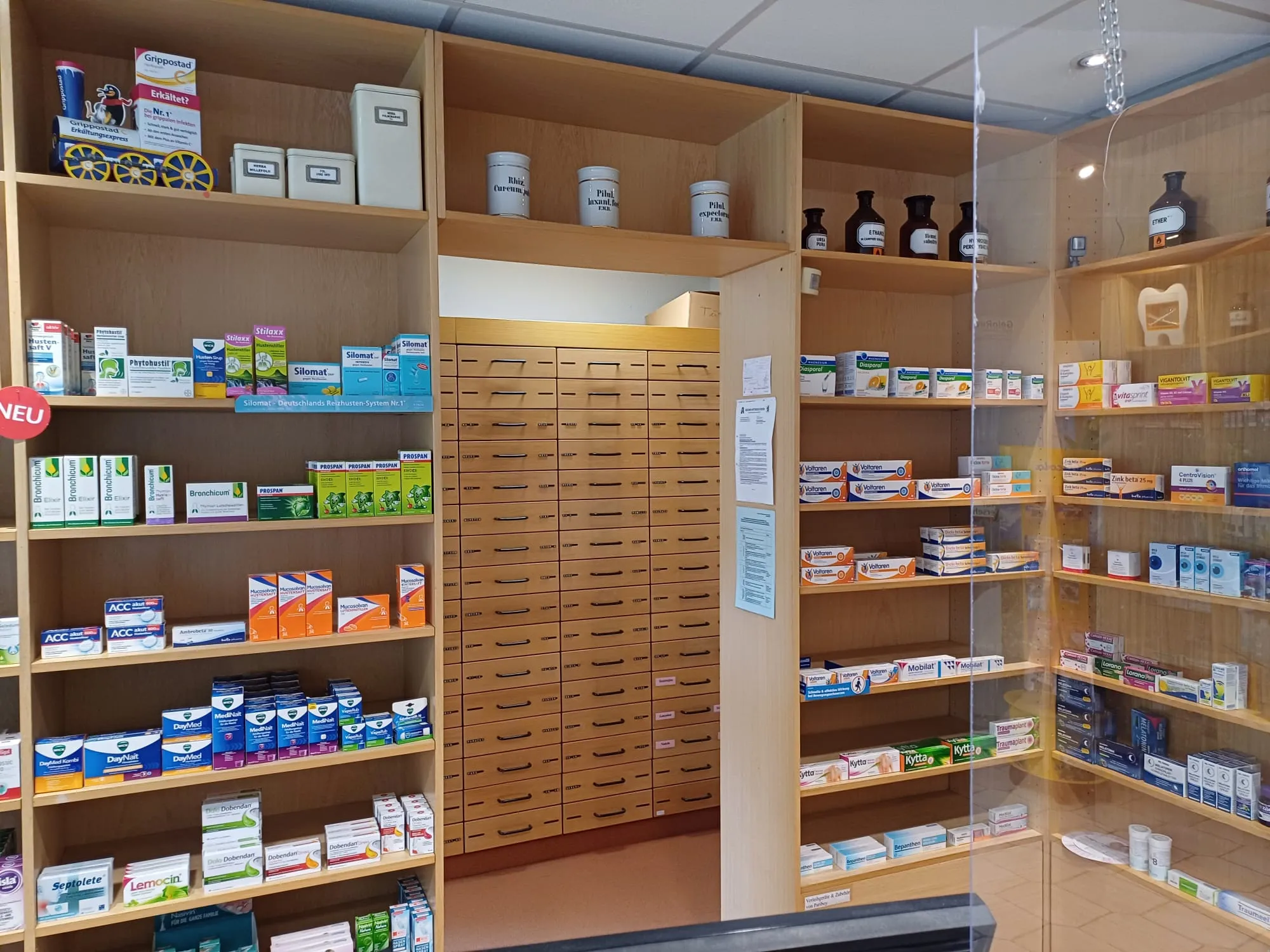 Verkaufsraum einer Apotheke mit Regalen voller Arzneimittelpackungen und einem Apothekerschrank mit vielen Schubladen