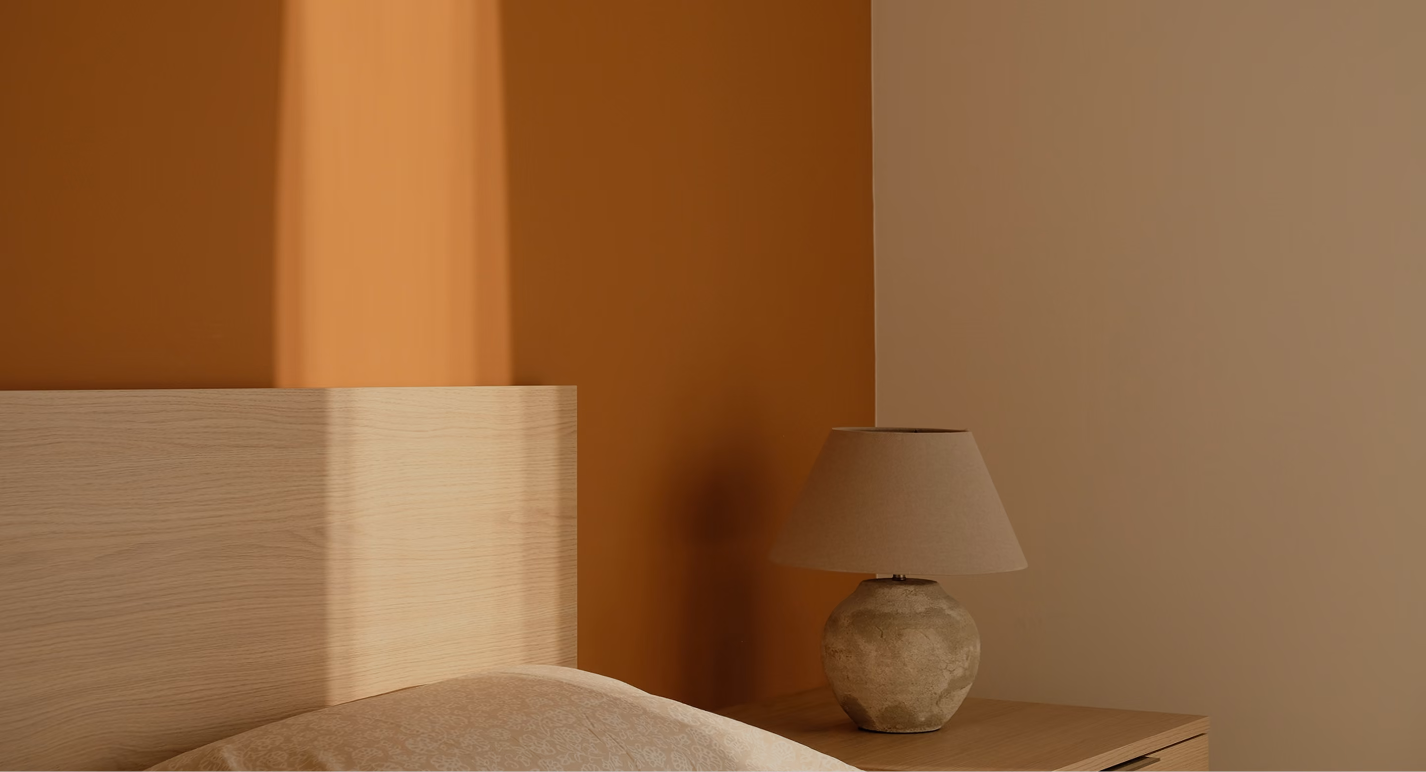 Bed with wooden headboard and beige lamp on wooden nightstand against two-toned brown wall.