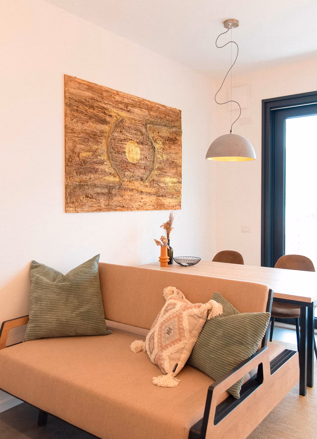 Modern living space with a beige couch, decorative pillows, abstract wall art, and a dining table with chairs.