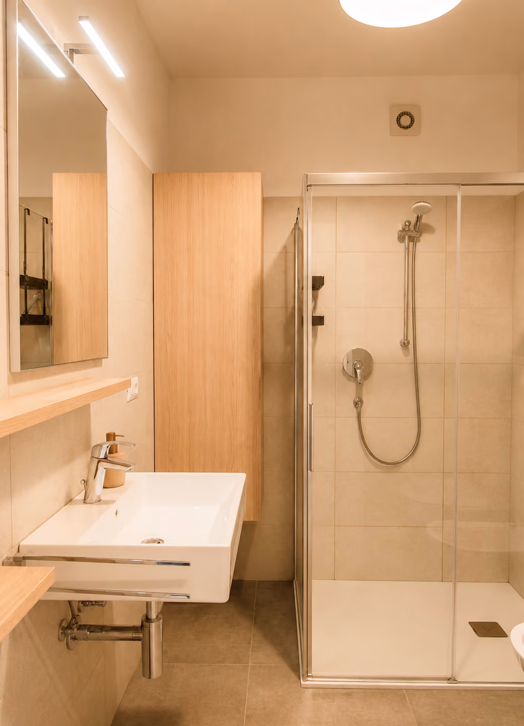 Minimalist bathroom with wall-mounted sink, wooden cabinet, and glass-enclosed shower with handheld showerhead.