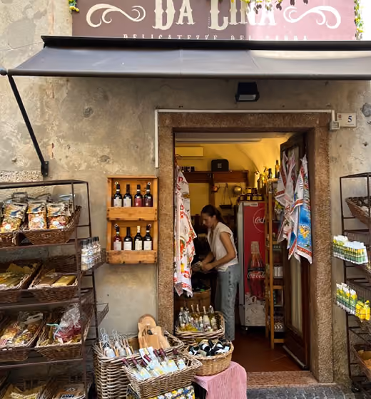 Small rustic store with shelves of food items and a woman inside near the doorway.