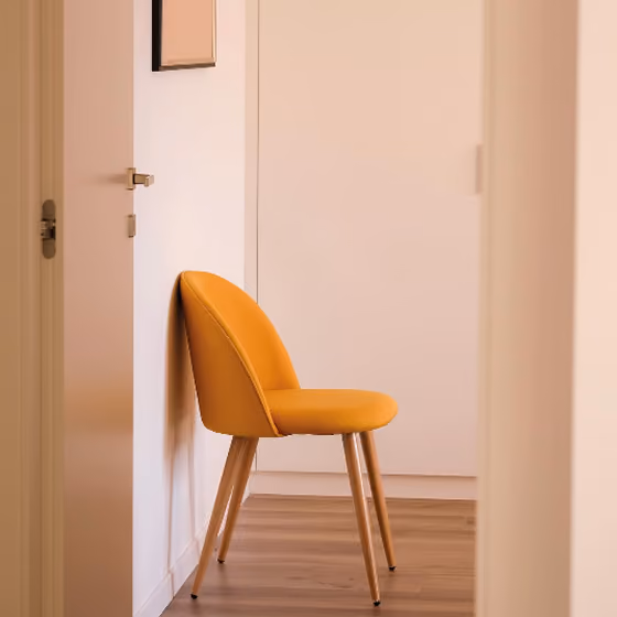 Yellow upholstered chair with wooden legs against a white wall on a hardwood floor.
