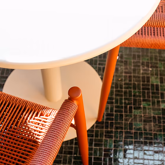 Top view of a white round table with orange woven chairs on a dark tiled floor.
