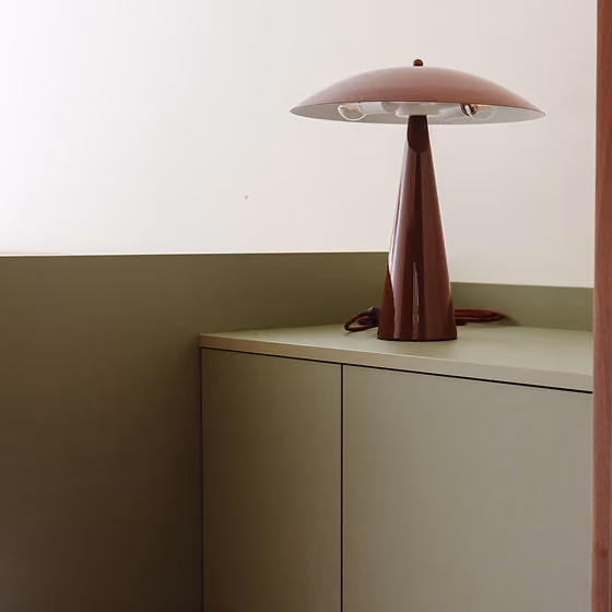 Modern brown mushroom-shaped table lamp on light green cabinet against white and olive wall.