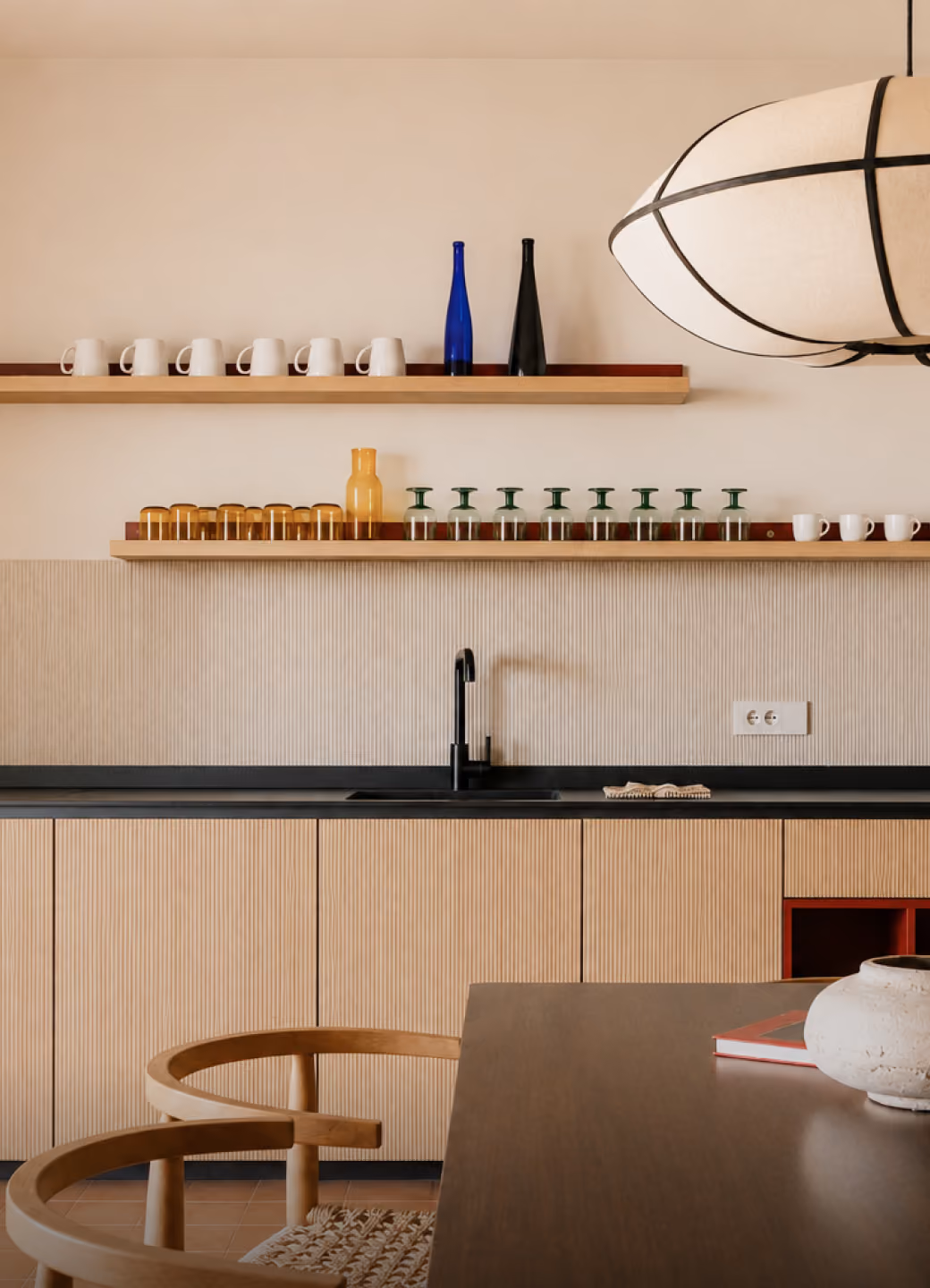 Minimalist kitchen with wooden cabinets, black faucet, open shelves holding mugs and glassware.