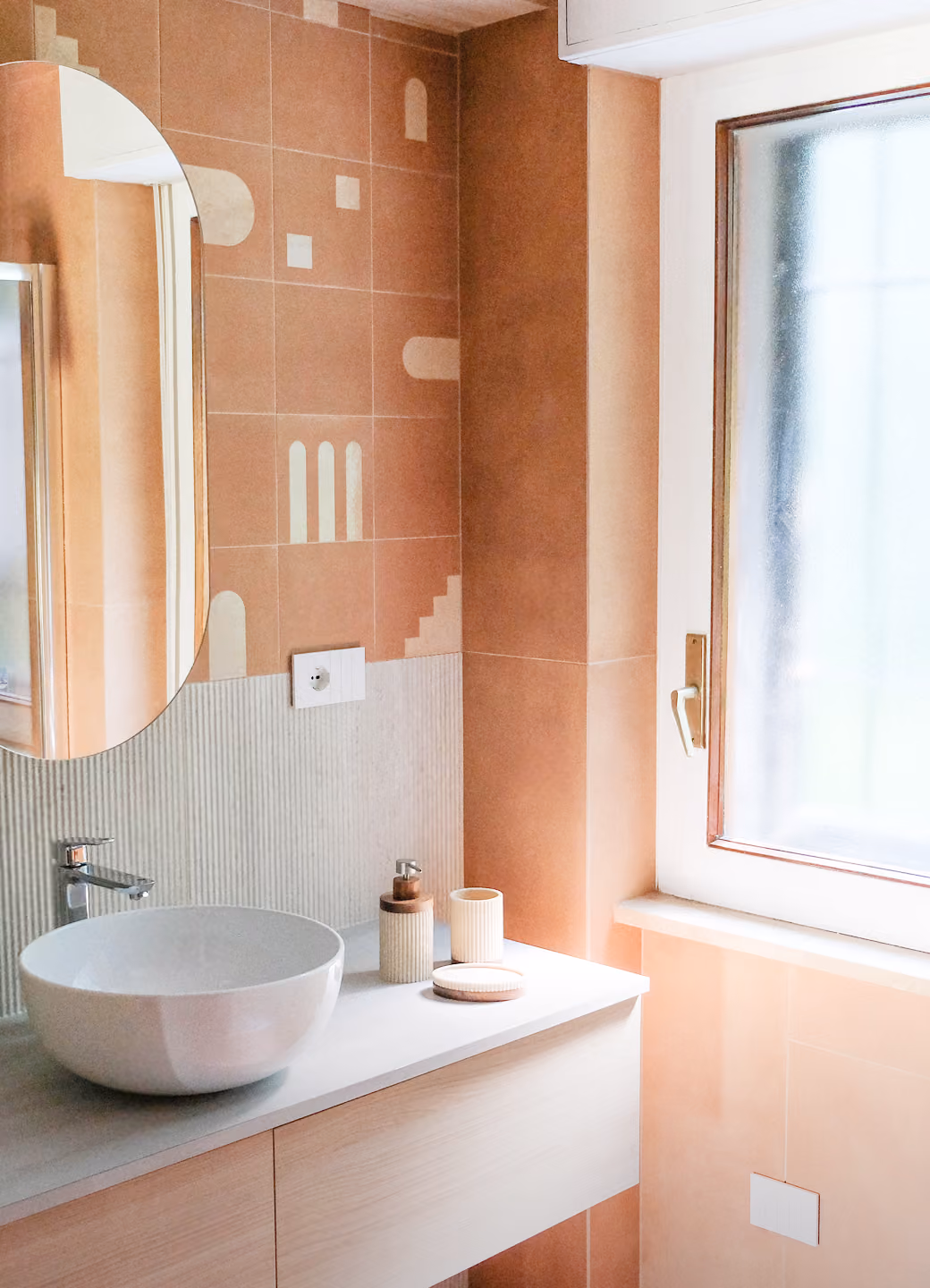 Modern bathroom with oval mirror, round white sink, soap dispenser, and frosted window.