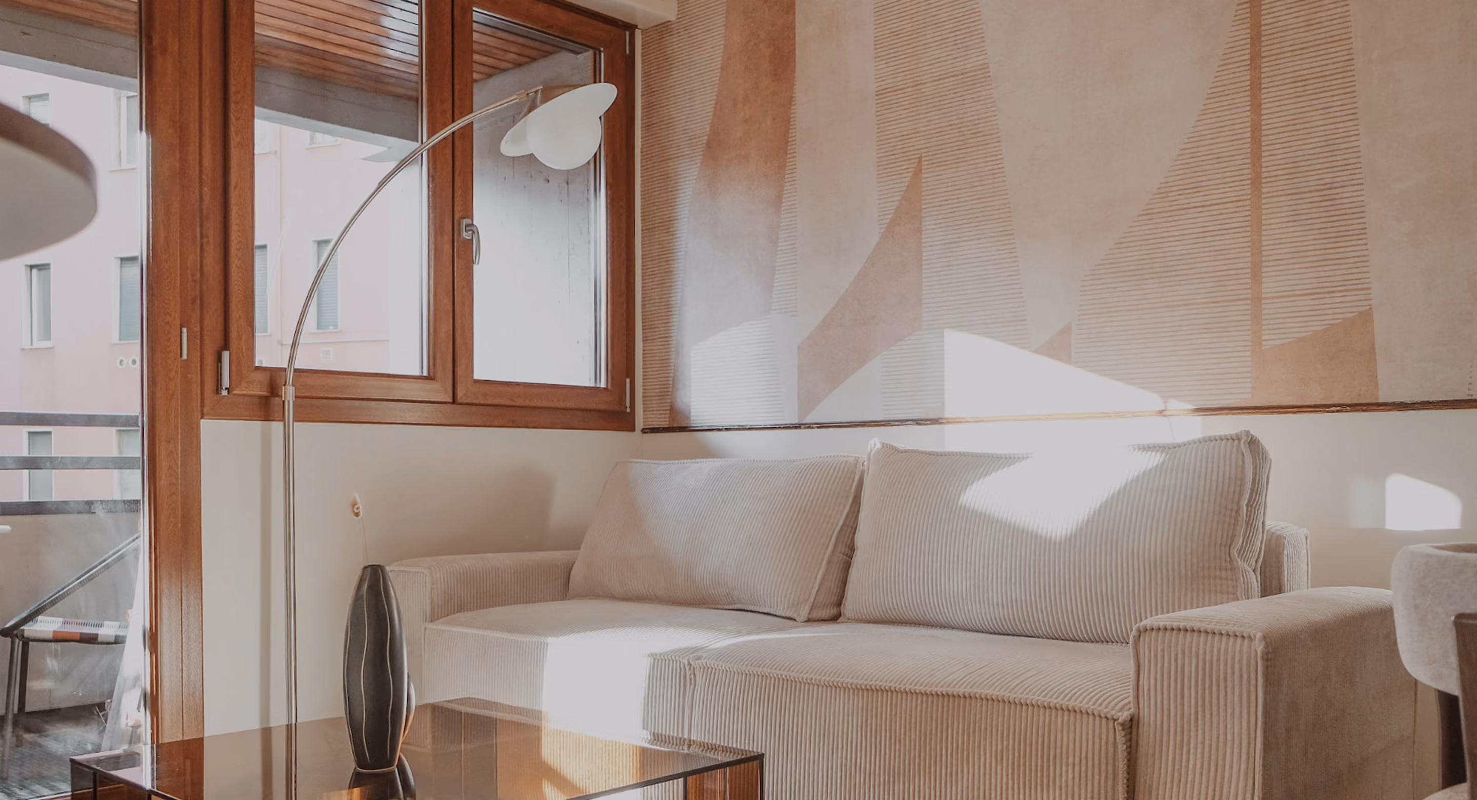 Beige corduroy sofa under abstract wall art with tall floor lamp near wooden framed windows.