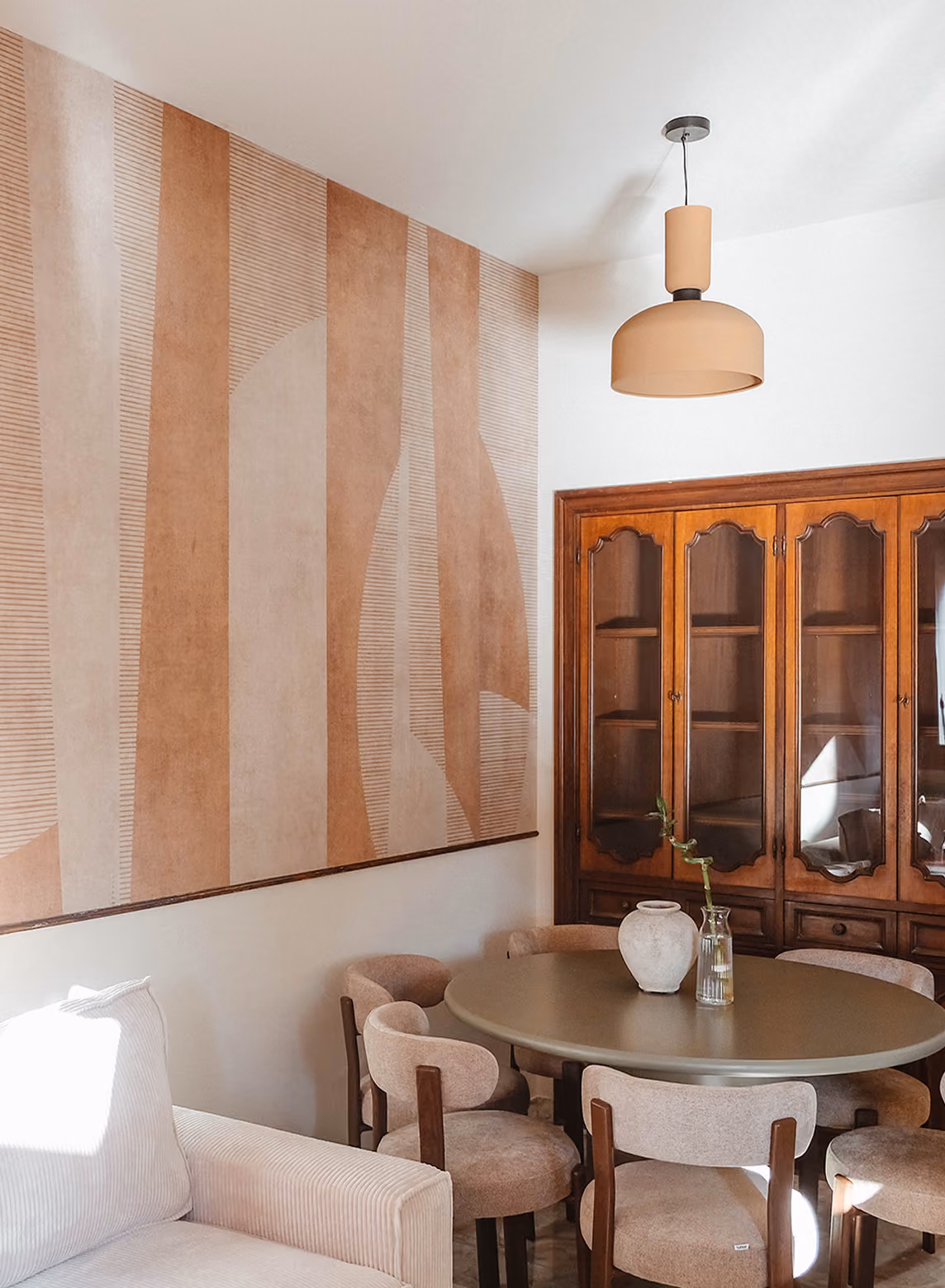 Dining area with a round table, six beige chairs, a wooden cabinet, and abstract wall art.