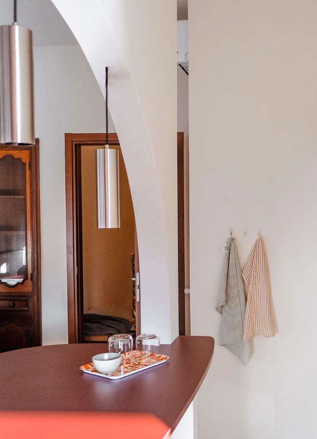 Table with tray holding a bowl and two glasses under hanging lights and next to arched doorway.