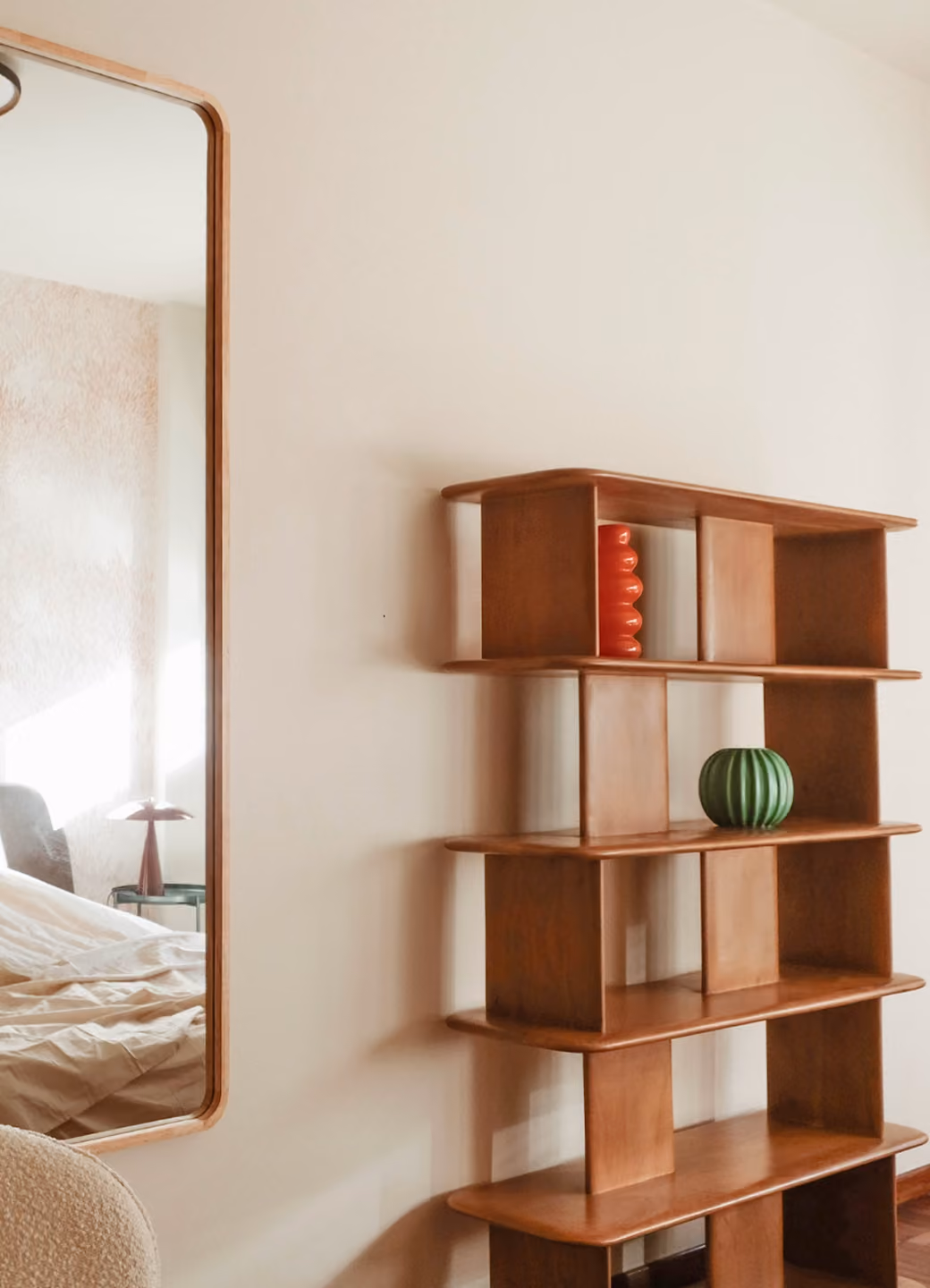 Modern wooden shelf with a red vase and green pumpkin-shaped decor, beside a large wall mirror.