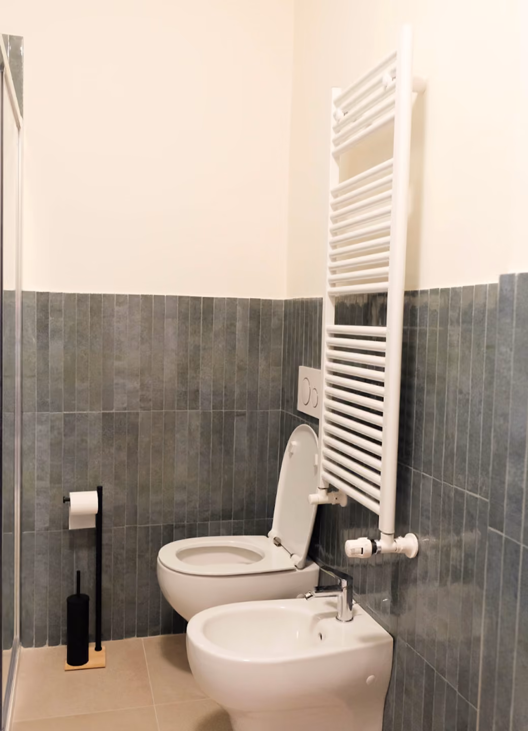 Modern bathroom with wall-mounted toilet, bidet, white towel radiator, and toilet brush holder.