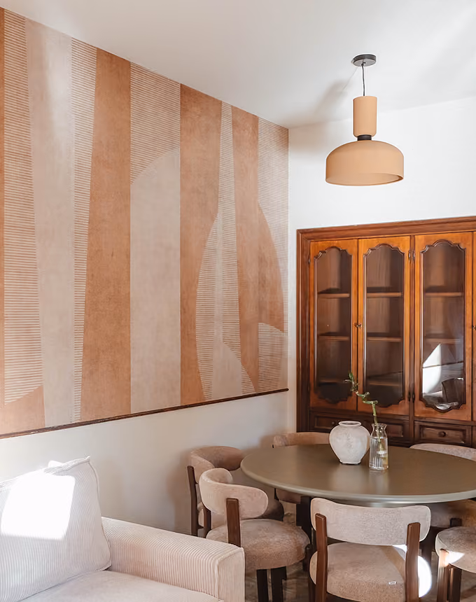 Cozy dining area with round table, beige chairs, patterned wood cabinet, pendant light, and abstract wall art.