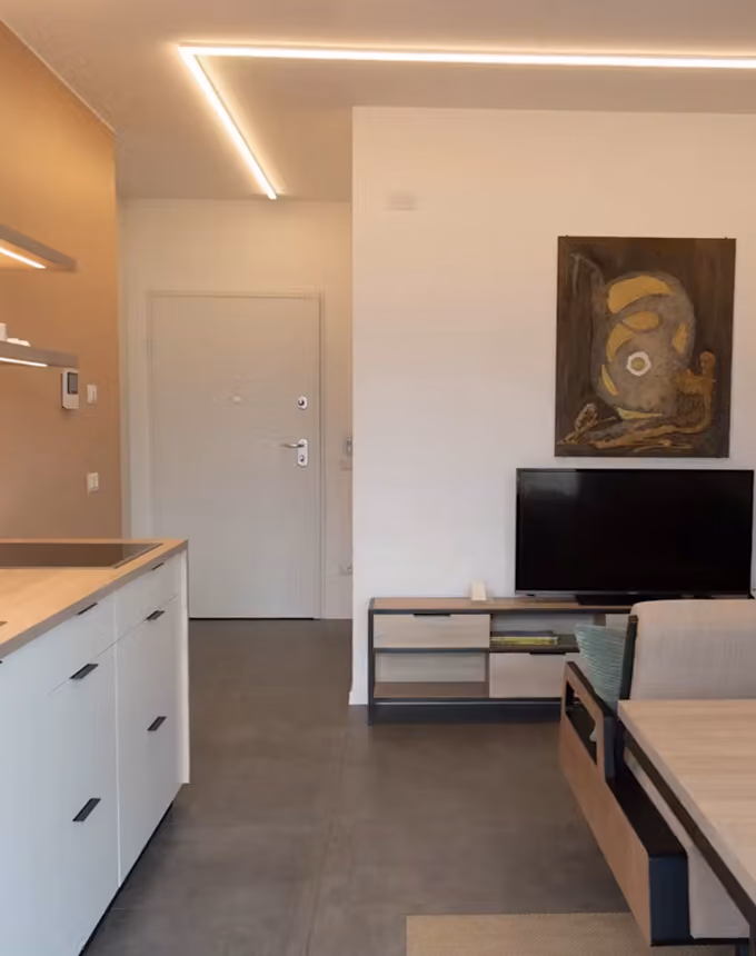 Minimalist living space with white kitchen cabinets, TV on a stand, and abstract art on white wall.