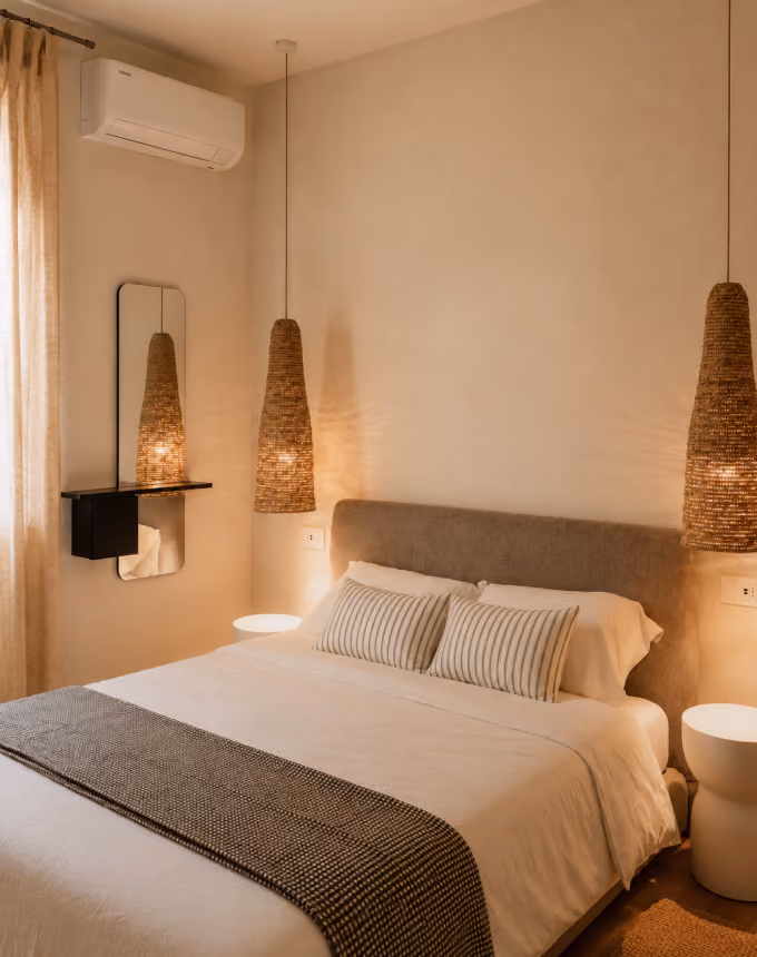 Cozy bedroom with a bed, striped pillows, woven pendant lights, and soft beige walls.